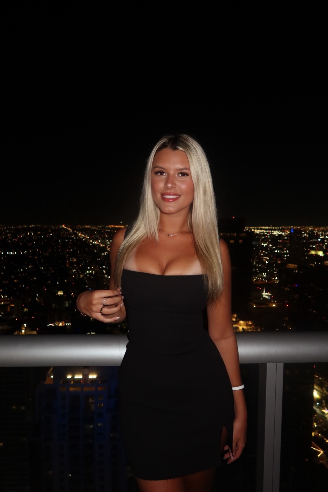 Averie in a black dress with a nighttime city skyline behind her