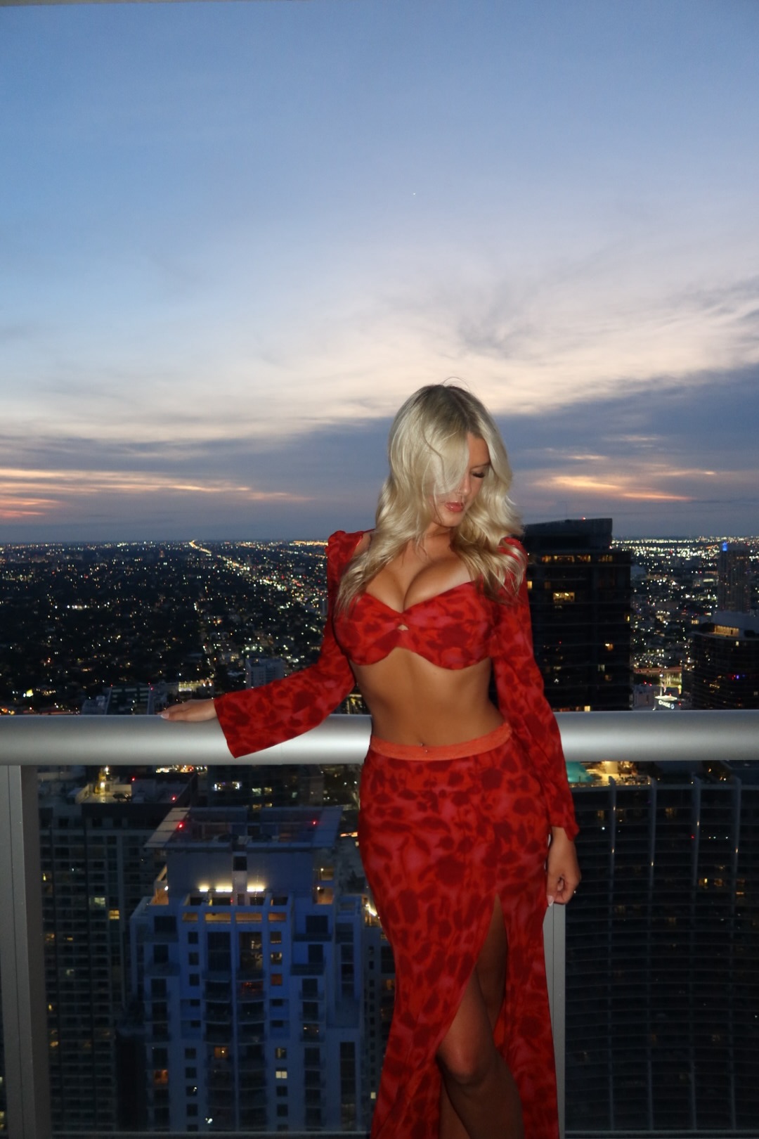 Averie looking down in a red two-piece fashion look on a city balcony